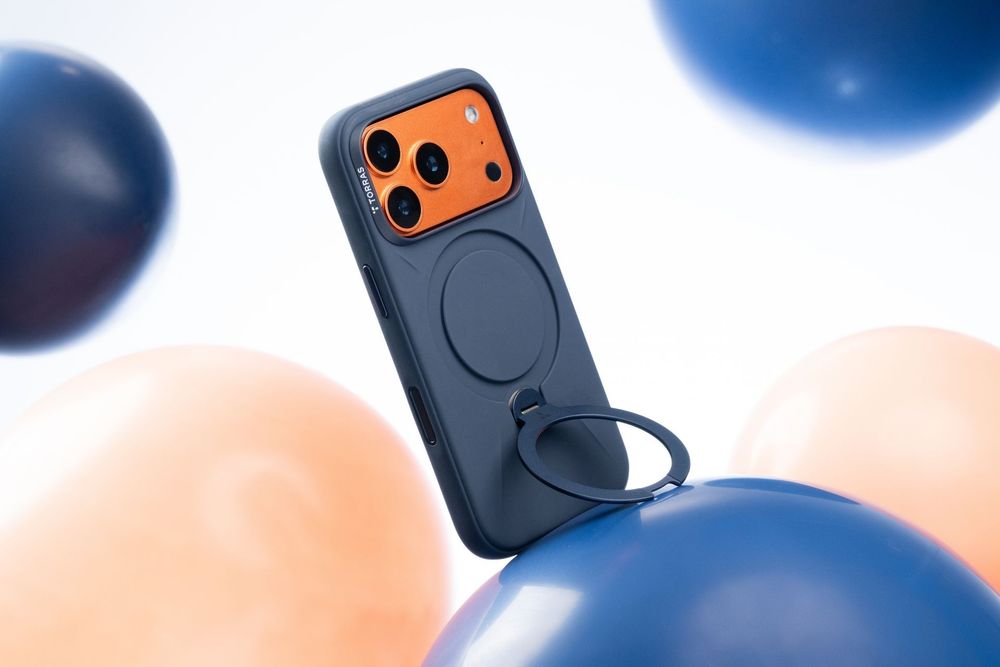 Navy blue iPhone case with orange camera panel and ring holder, surrounded by colorful balloons on white background.