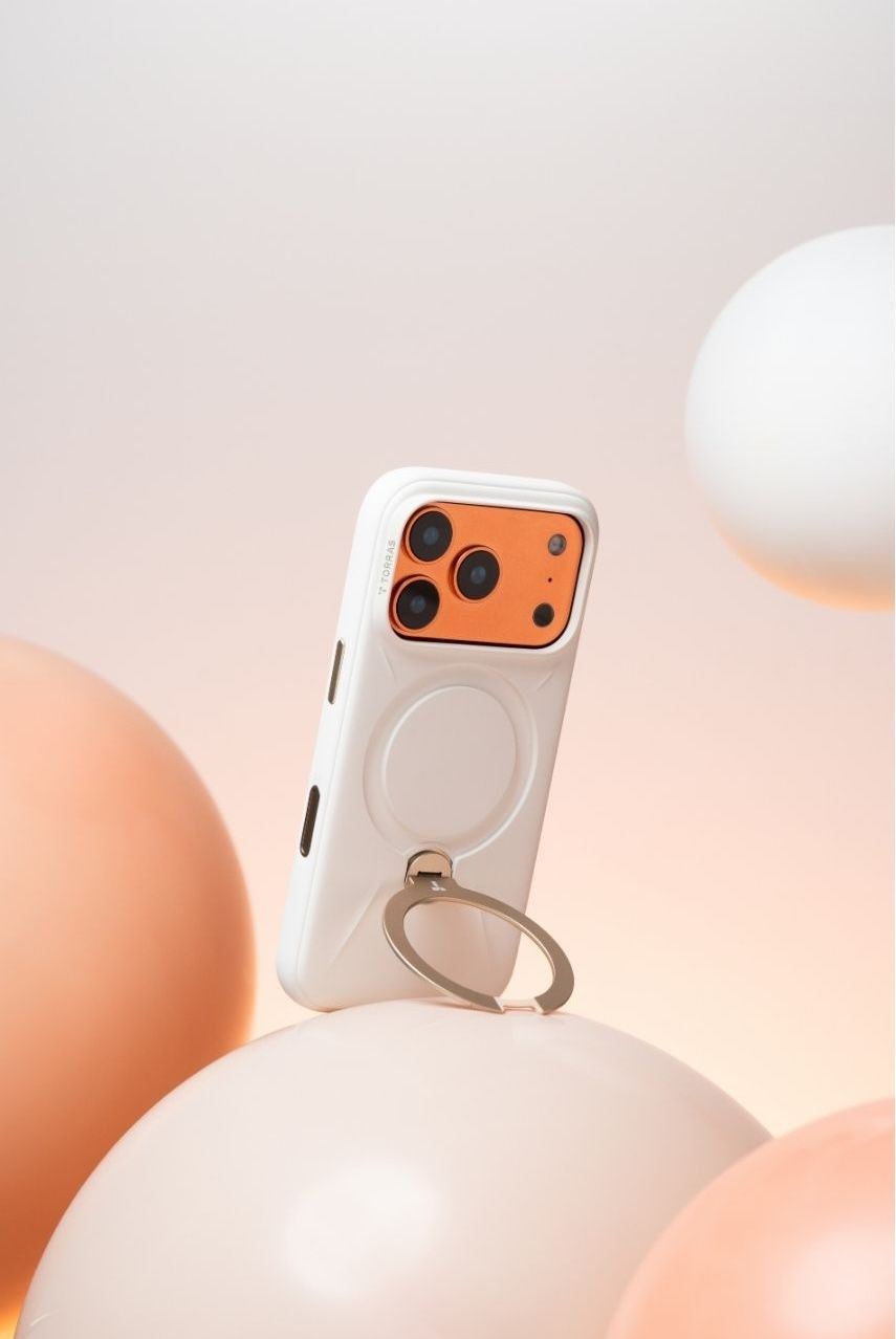 White iPhone case with orange camera surround, MagSafe ring holder, displayed on peach balloons.