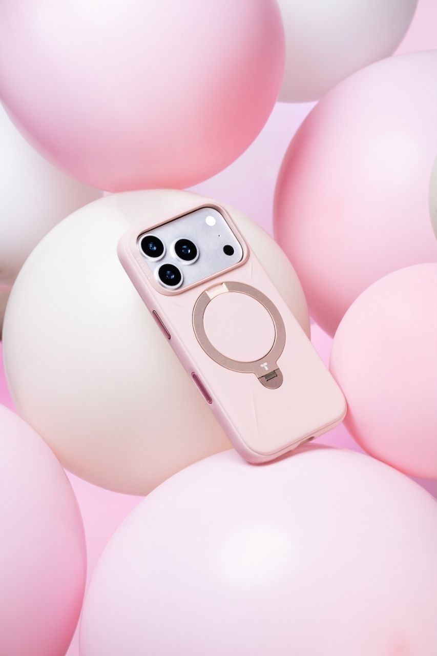 Pink iPhone case with MagSafe ring stand surrounded by pink and white balloons on a soft pink background.