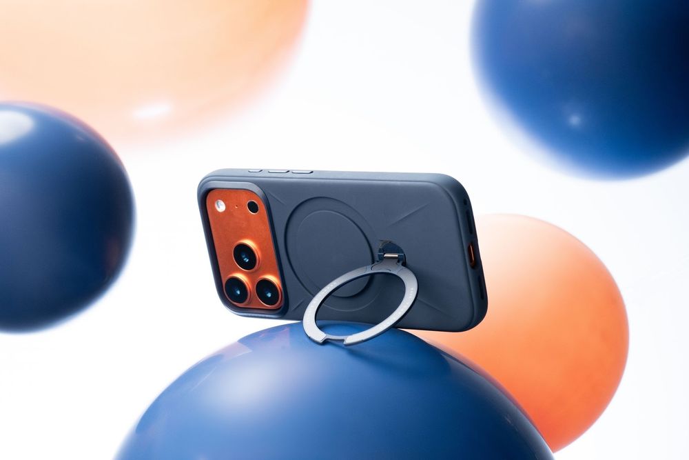 Dark blue iPhone case with ring stand balanced on navy balloon surrounded by blue and orange balloons.