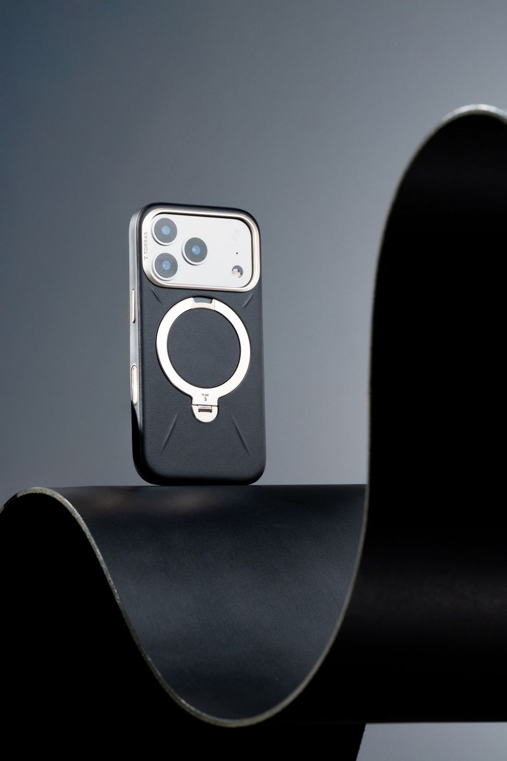 Black iPhone case with MagSafe ring stand displayed on curved dark surface.