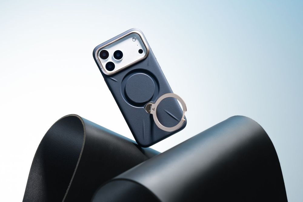 Dark blue iPhone case with MagSafe ring holder displayed on curved black surface against light blue background.