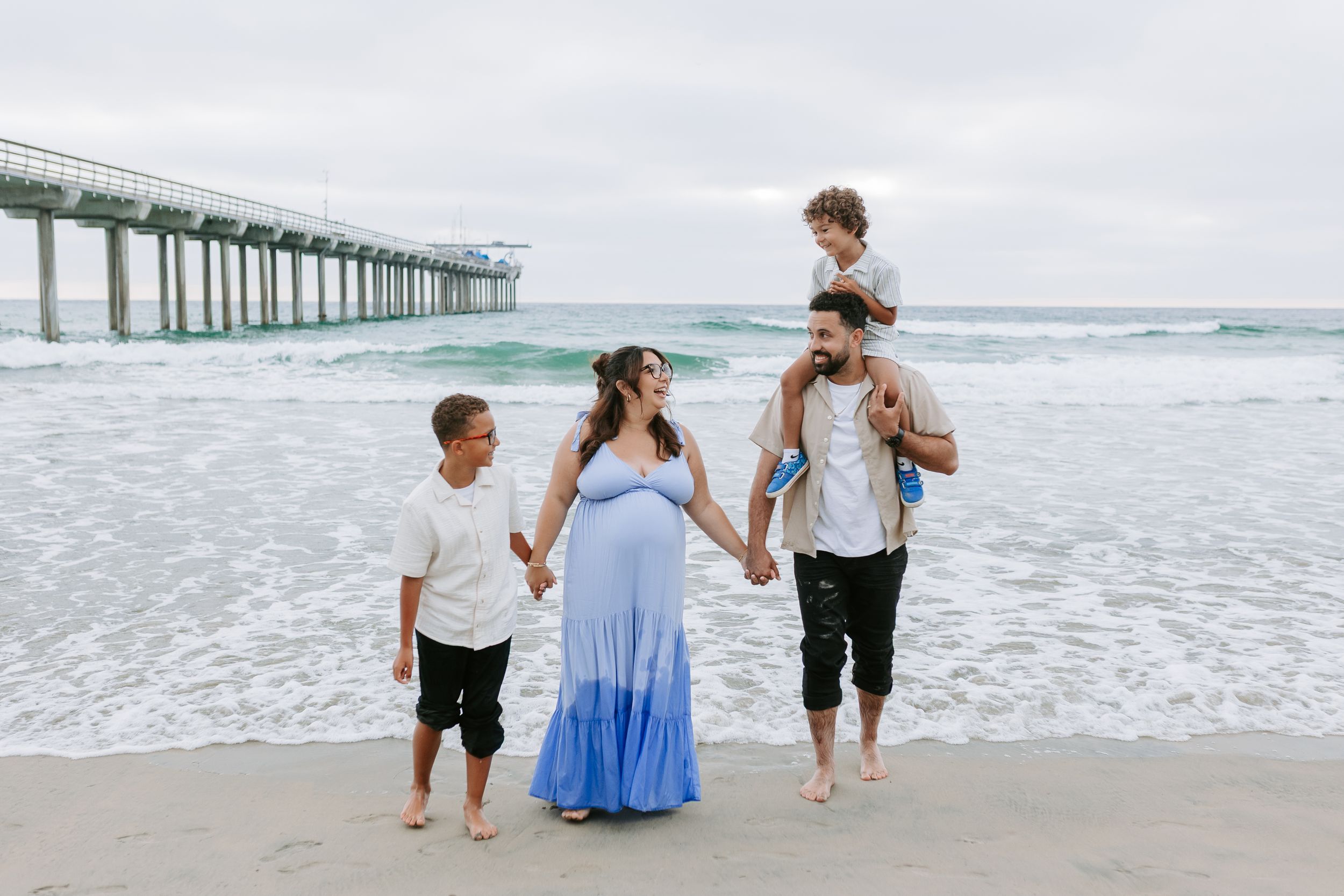 A family of four walks along a beach in San Diego holding hands.