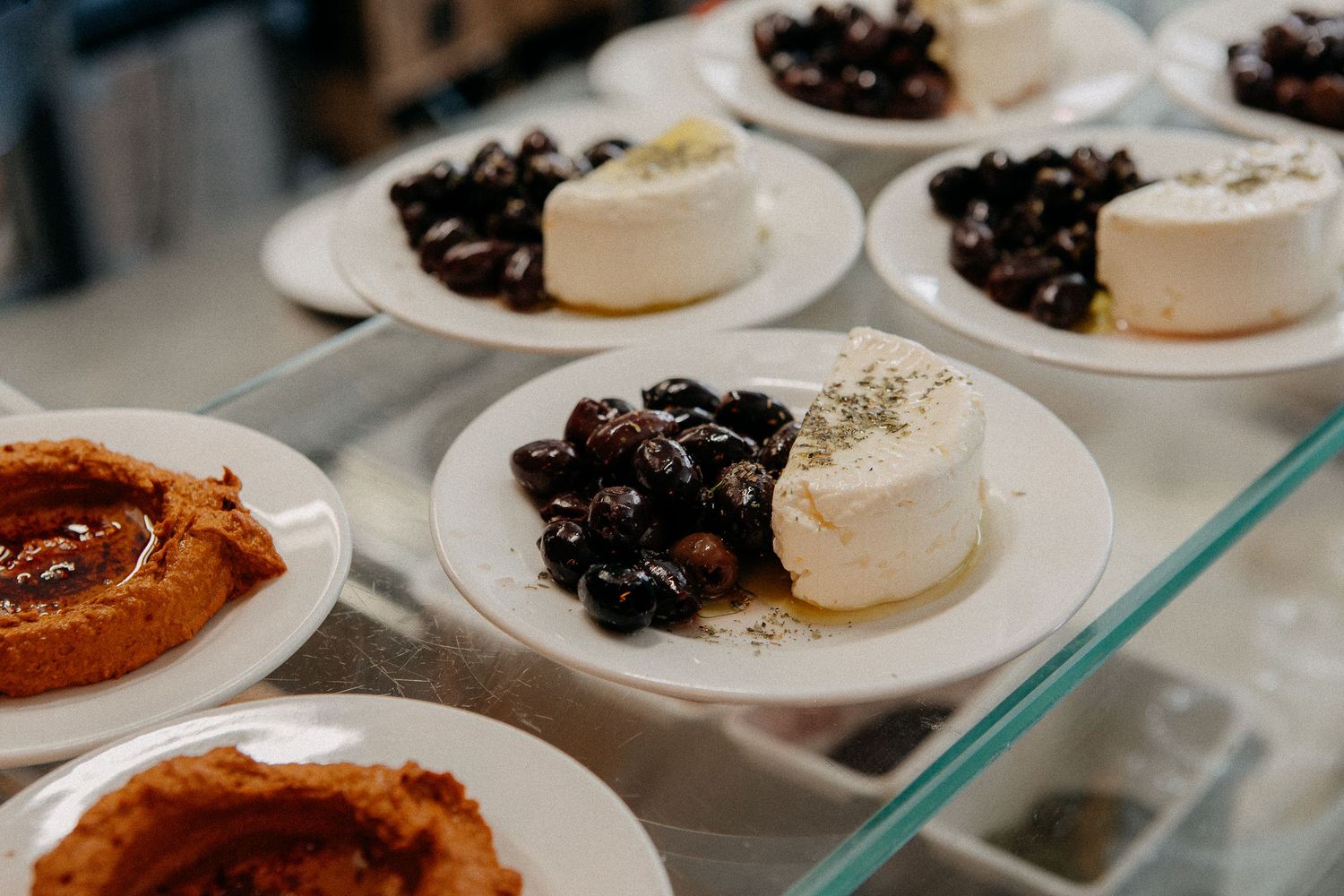 White plates display fresh feta cheese topped with marinated black olives, served as appetizers in a Mediterranean restaurant.