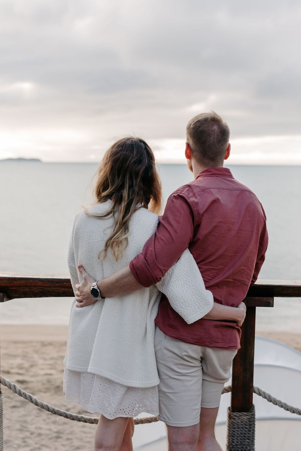 Couple embracing while gazing at ocean view from beach deck at sunset.