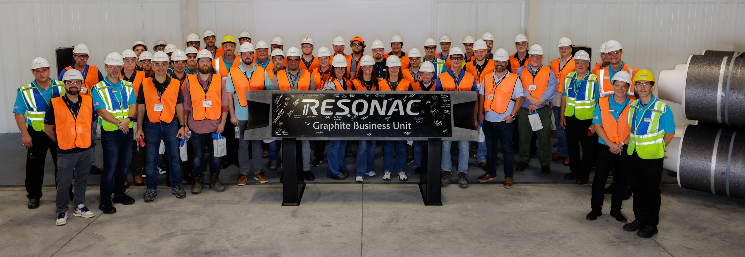 Large group of workers in safety gear and hard hats lined up at an industrial facility.