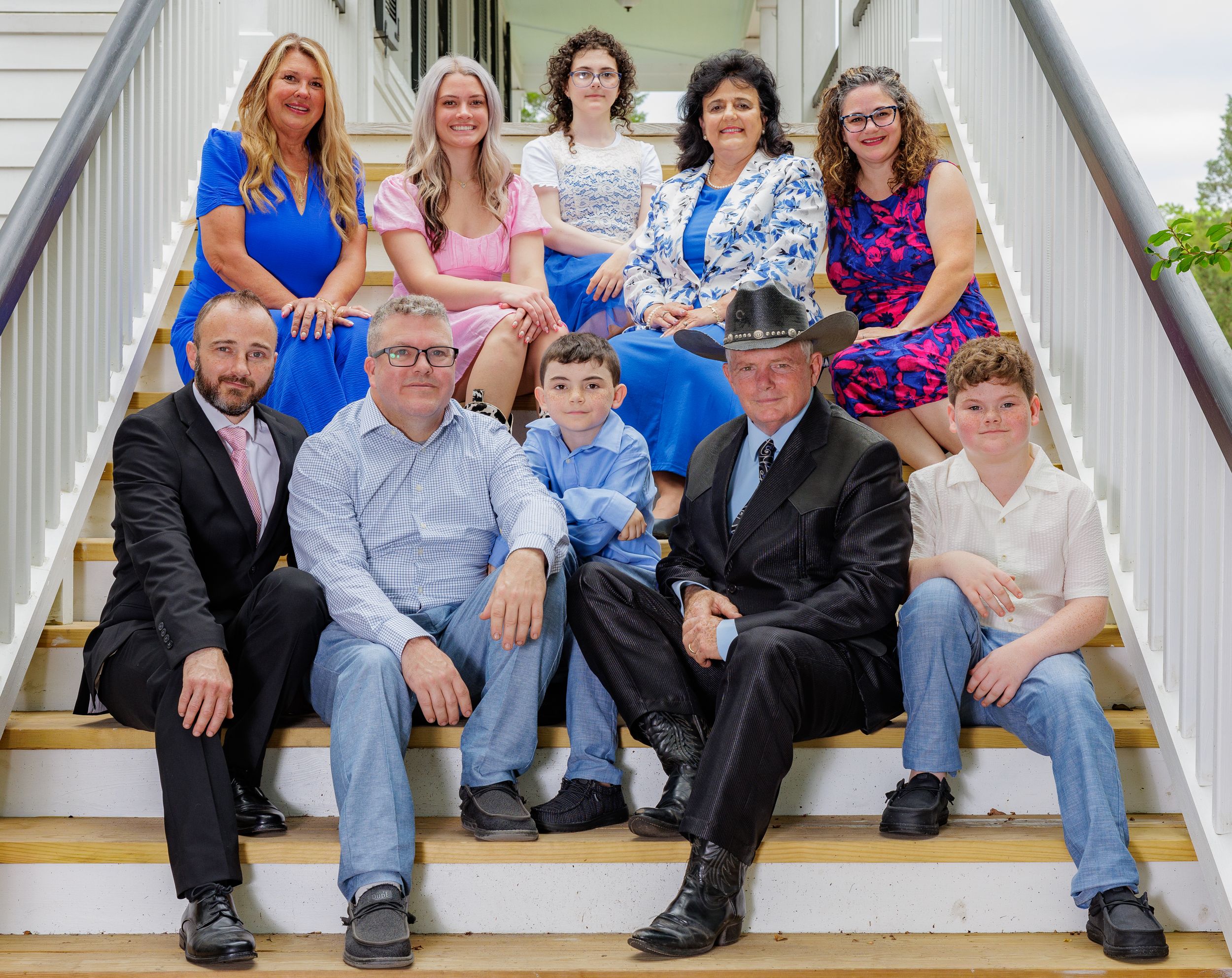 A large family group poses together on outdoor white stairs for a formal portrait.