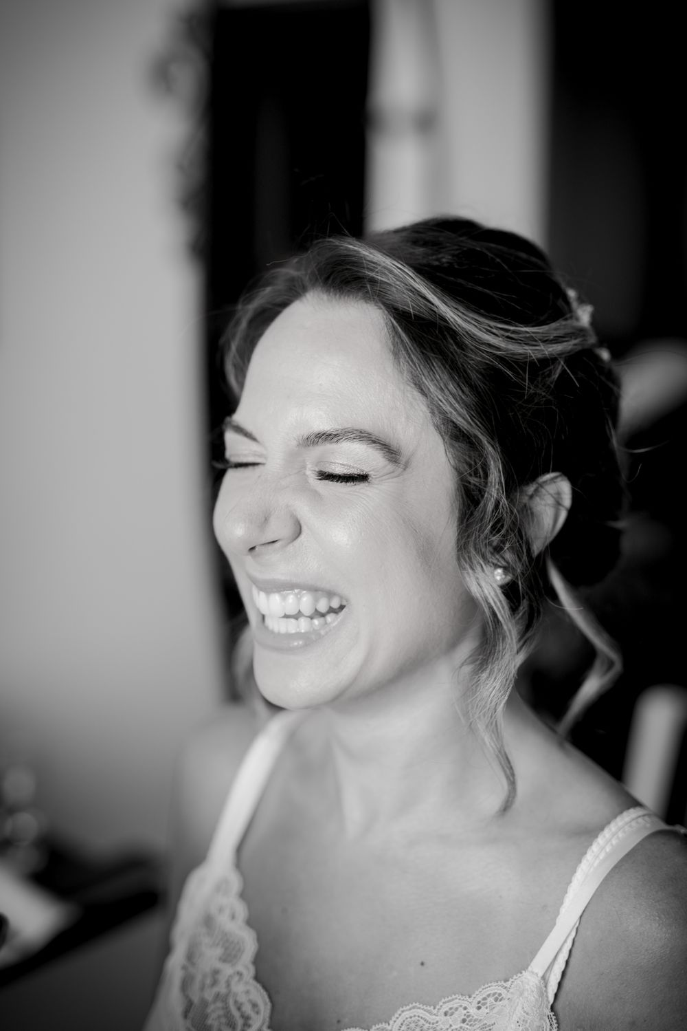 Black and white portrait of a laughing bride during wedding preparations with eyes closed.