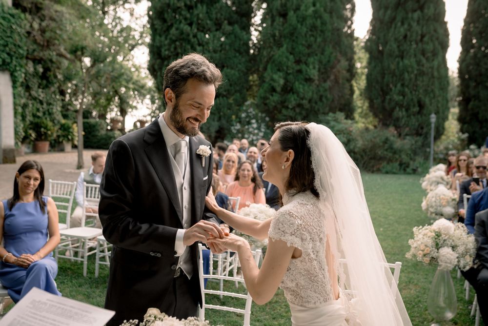 Groom smiling while placing a ring on the bride's finger during an outdoor garden ceremony.