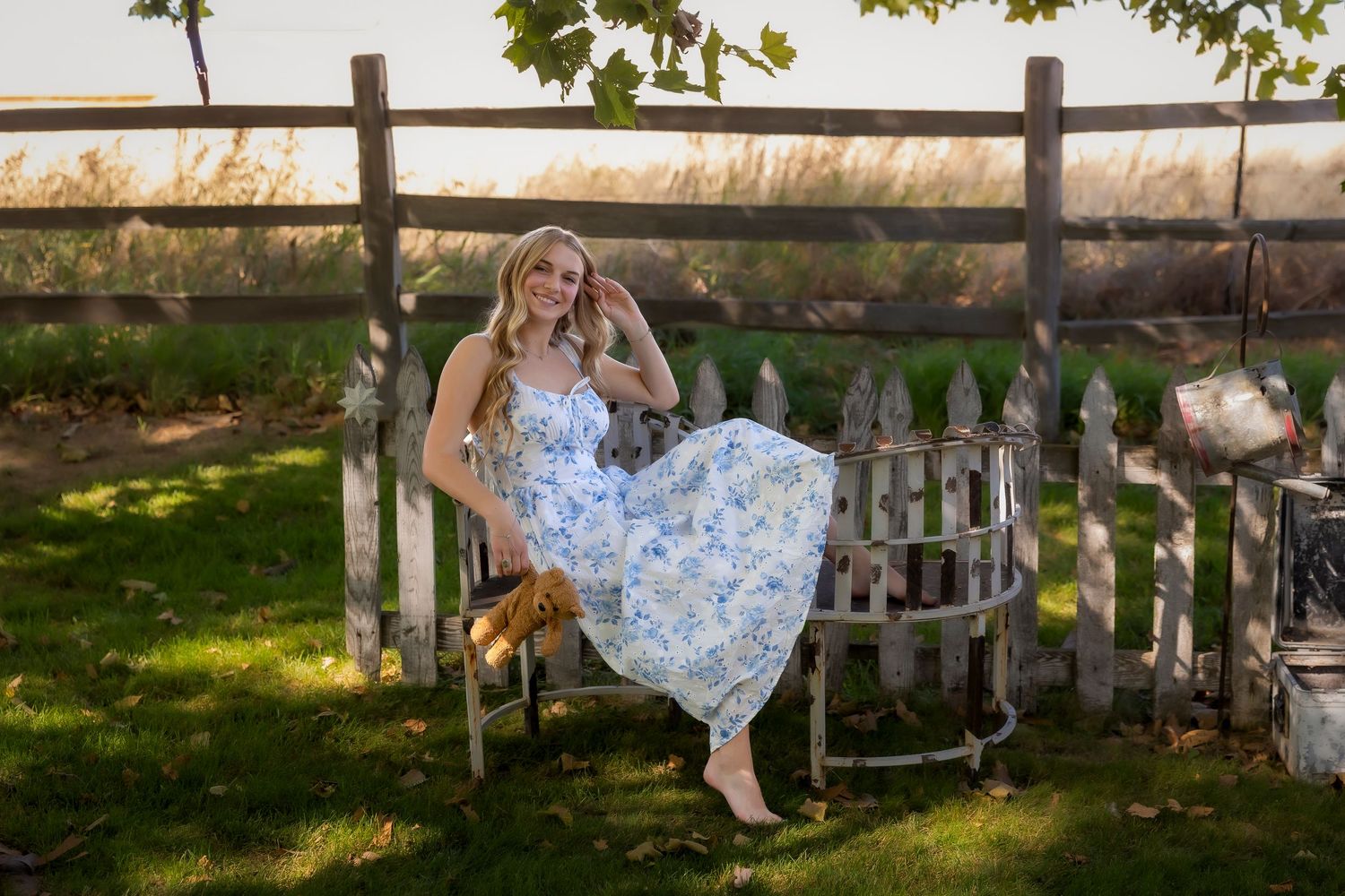 girl in blue and white floral dress sitting on conversation bench with teddy bear