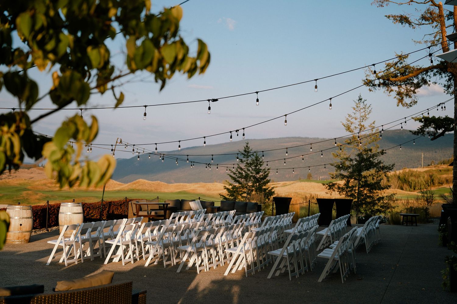 Outdoor wedding ceremony setup with white chairs, string lights, and scenic rolling hills backdrop at golden hour.
