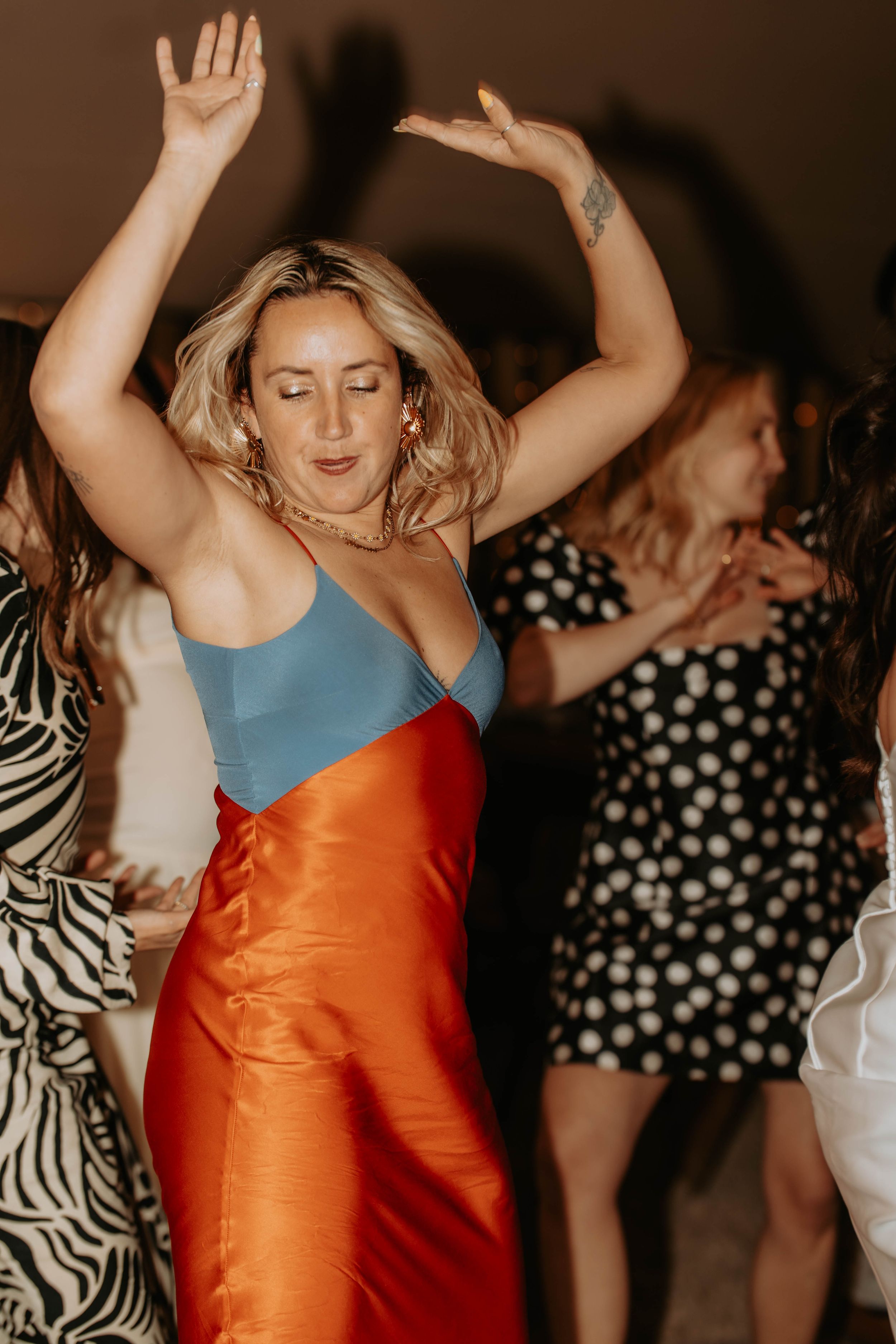 Woman in blue and orange satin dress dancing with arms raised at a party.