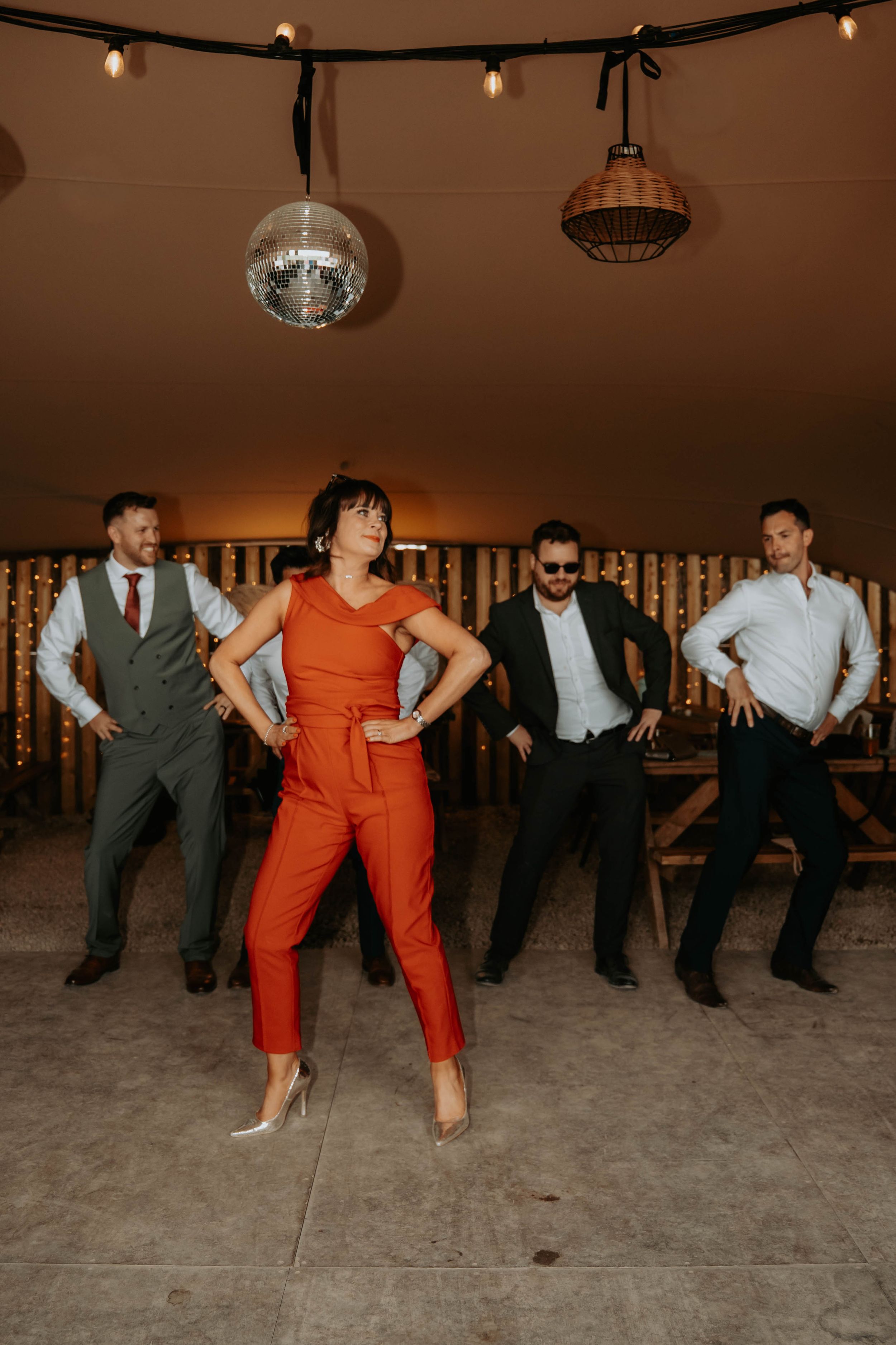 Group of four people dancing at a party venue with disco ball and string lights overhead.