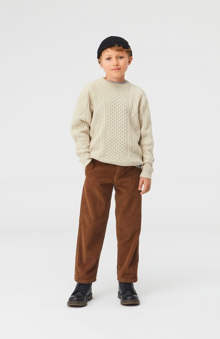 Boy wearing a beige cable-knit sweater, brown corduroy pants, black cap, and black shoes.