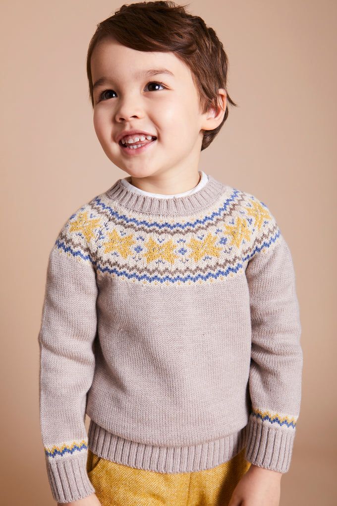 Smiling toddler boy wearing a gray Fair Isle knit sweater with yellow and blue pattern details.