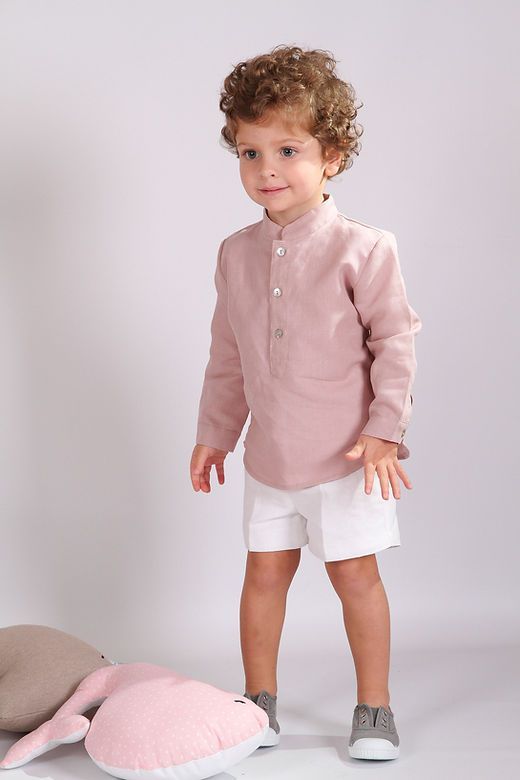 Young boy in pink linen mandarin collar shirt with white shorts and gray sneakers.
