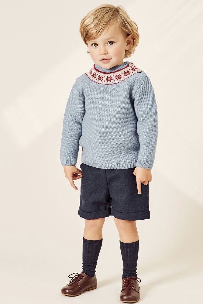 Toddler boy wearing a light blue Fair Isle knit sweater, navy shorts, knee socks, and brown leather shoes.