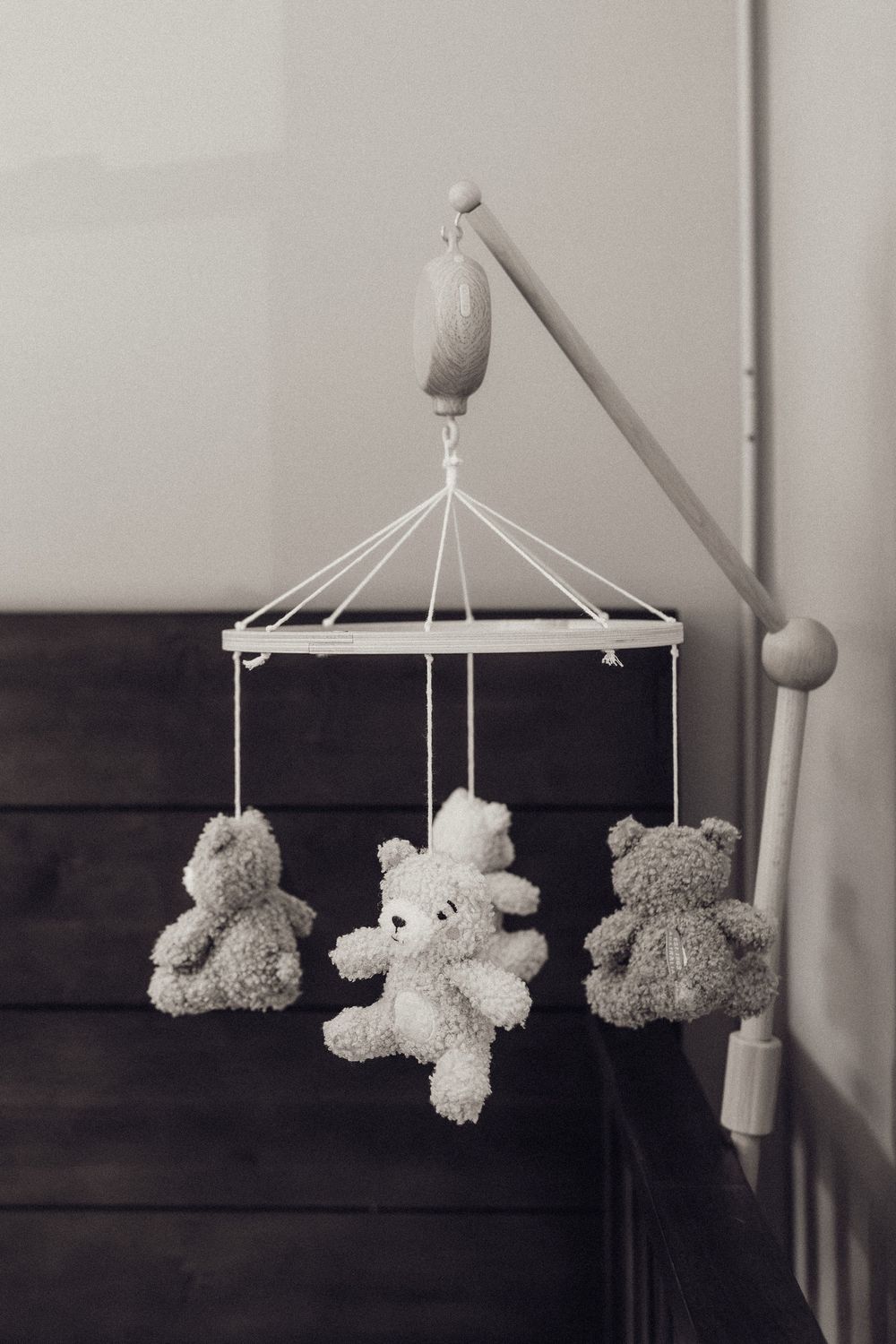 Black and white photo of a baby crib mobile with three soft teddy bear plush toys.