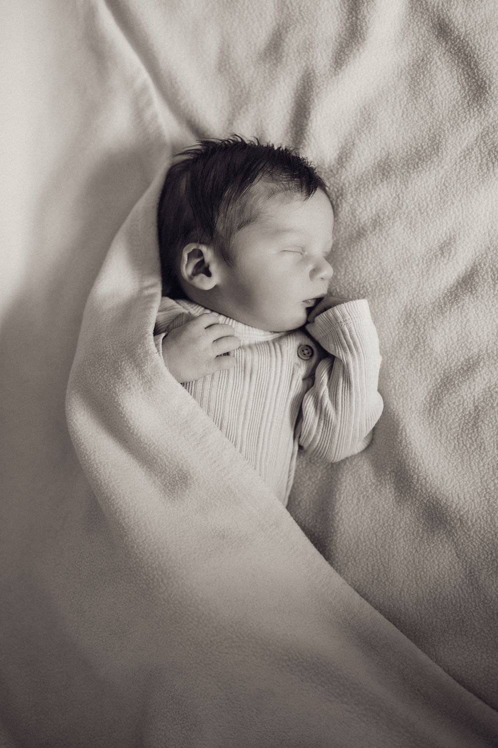 Serene newborn baby sleeping wrapped in soft white blanket in black and white photo.