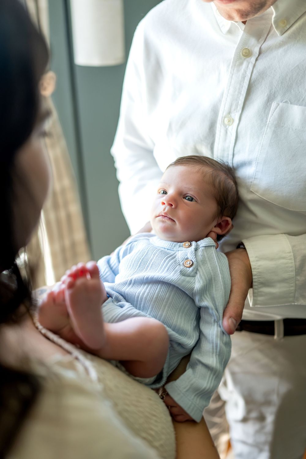 Newborn baby in blue outfit cradled in fathers arms during in-home photo session.