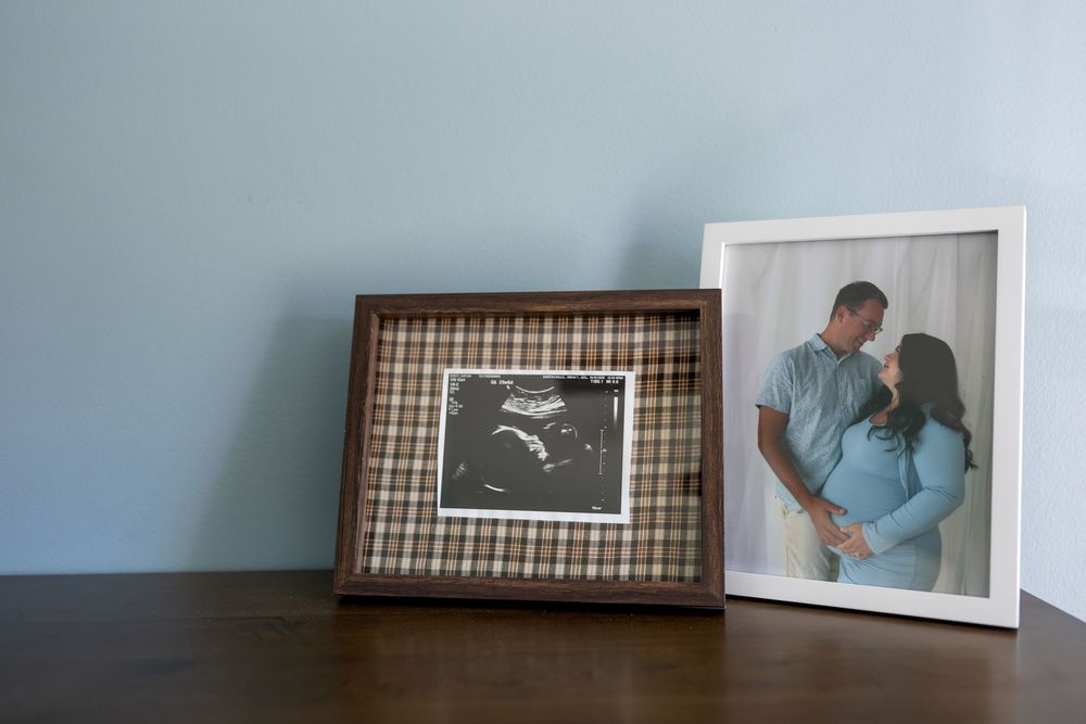 Two framed photos on a wooden dresser featuring an ultrasound and a maternity couple portrait against a blue wall.