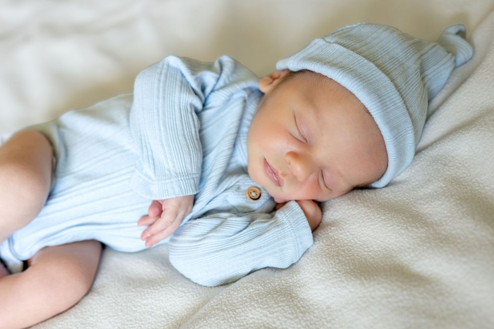 Peaceful newborn baby sleeping in a blue outfit and matching hat on a soft blanket.