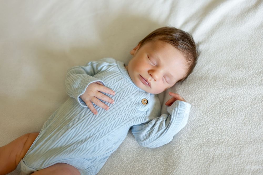 Peaceful newborn baby sleeping in light blue striped onesie on soft white blanket.