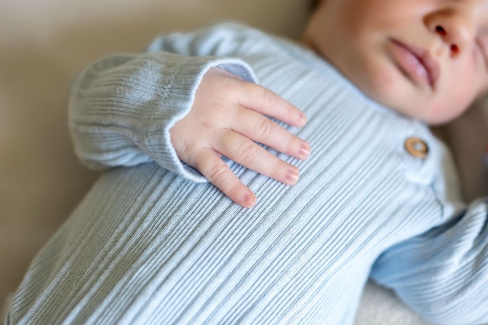 Close-up of a newborn baby's tiny hand resting on a soft blue knit outfit.