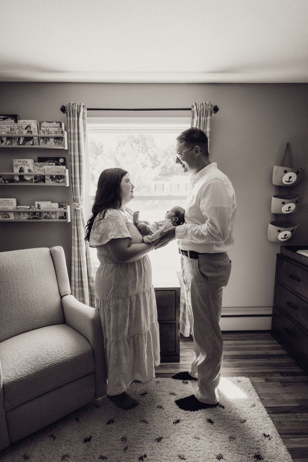 Black and white photo of new parents sharing a tender moment with newborn in nursery.