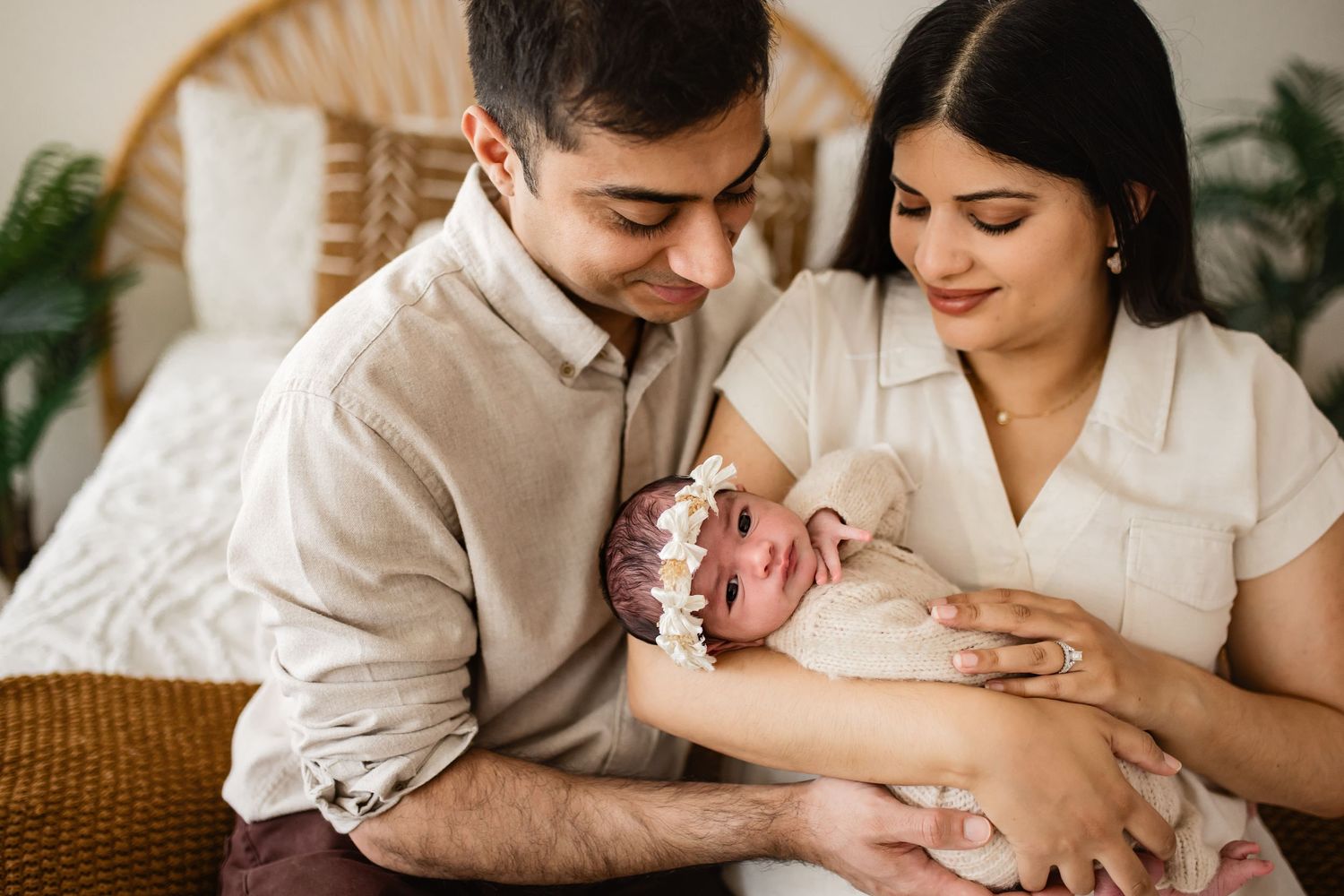 New parents lovingly cradle their newborn baby, sharing a tender family moment in a warm, cozy bedroom setting.