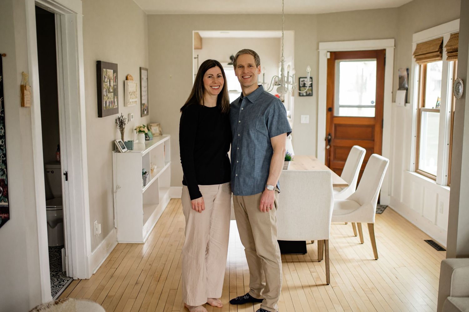 Couple smiling together in a bright, modern home interior with hardwood floors and dining area.