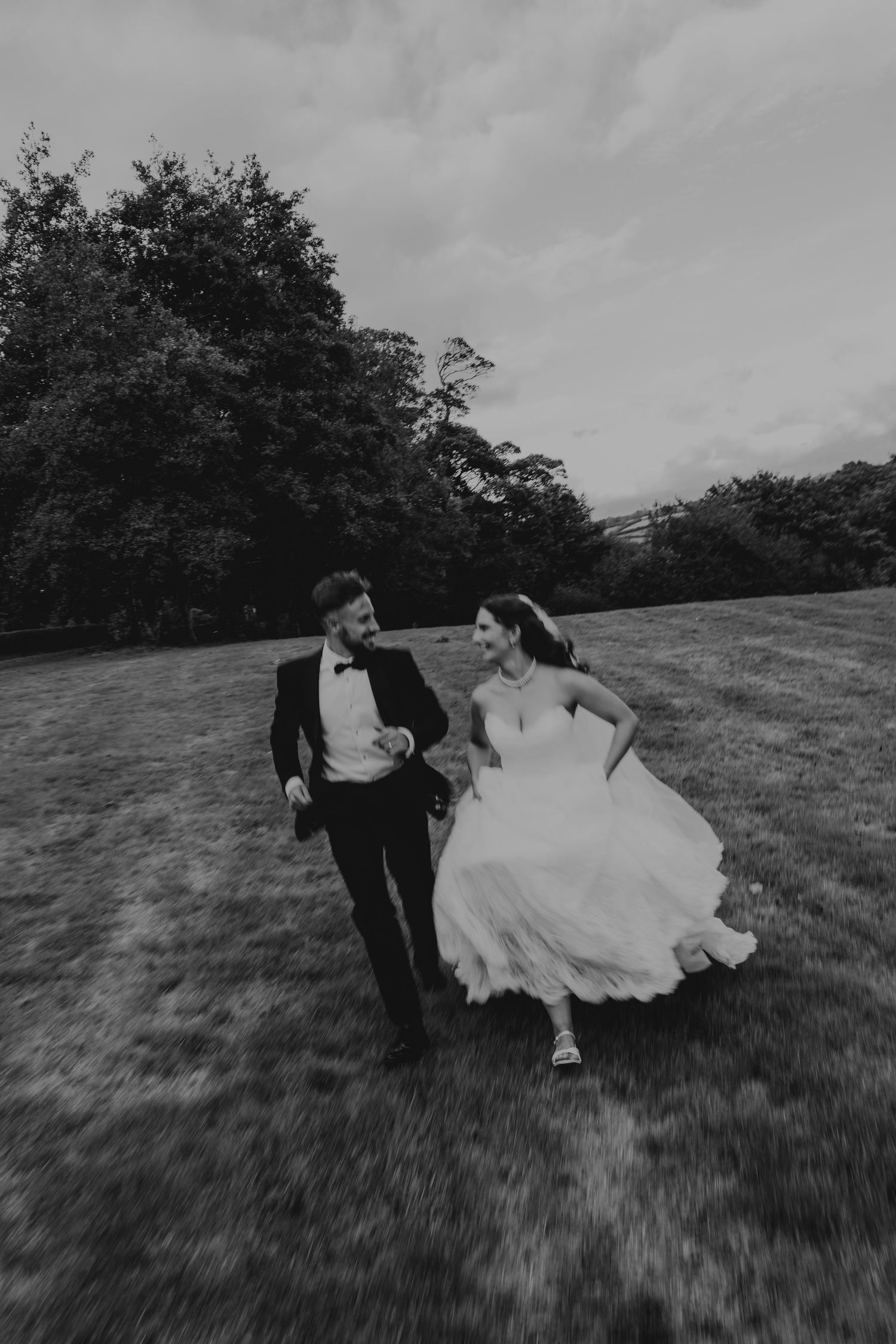 Black and white photo of bride and groom running joyfully through a grassy field on their wedding dayat The Green wedding venue.