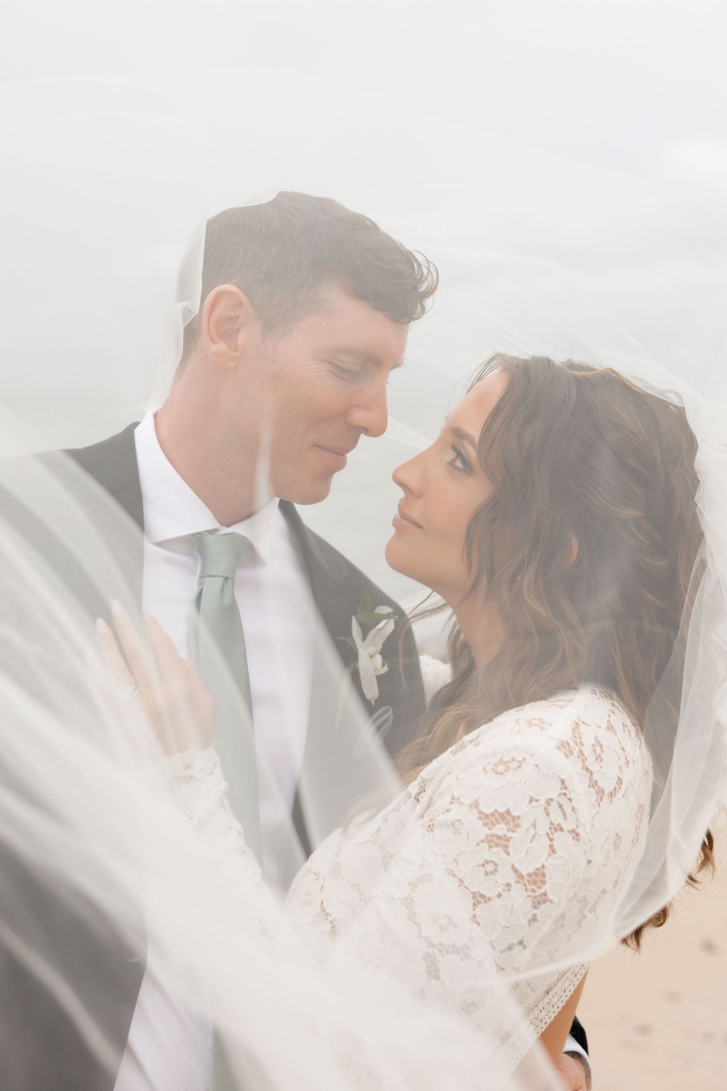 Bride and groom share an intimate moment under a flowing veil on their wedding day.