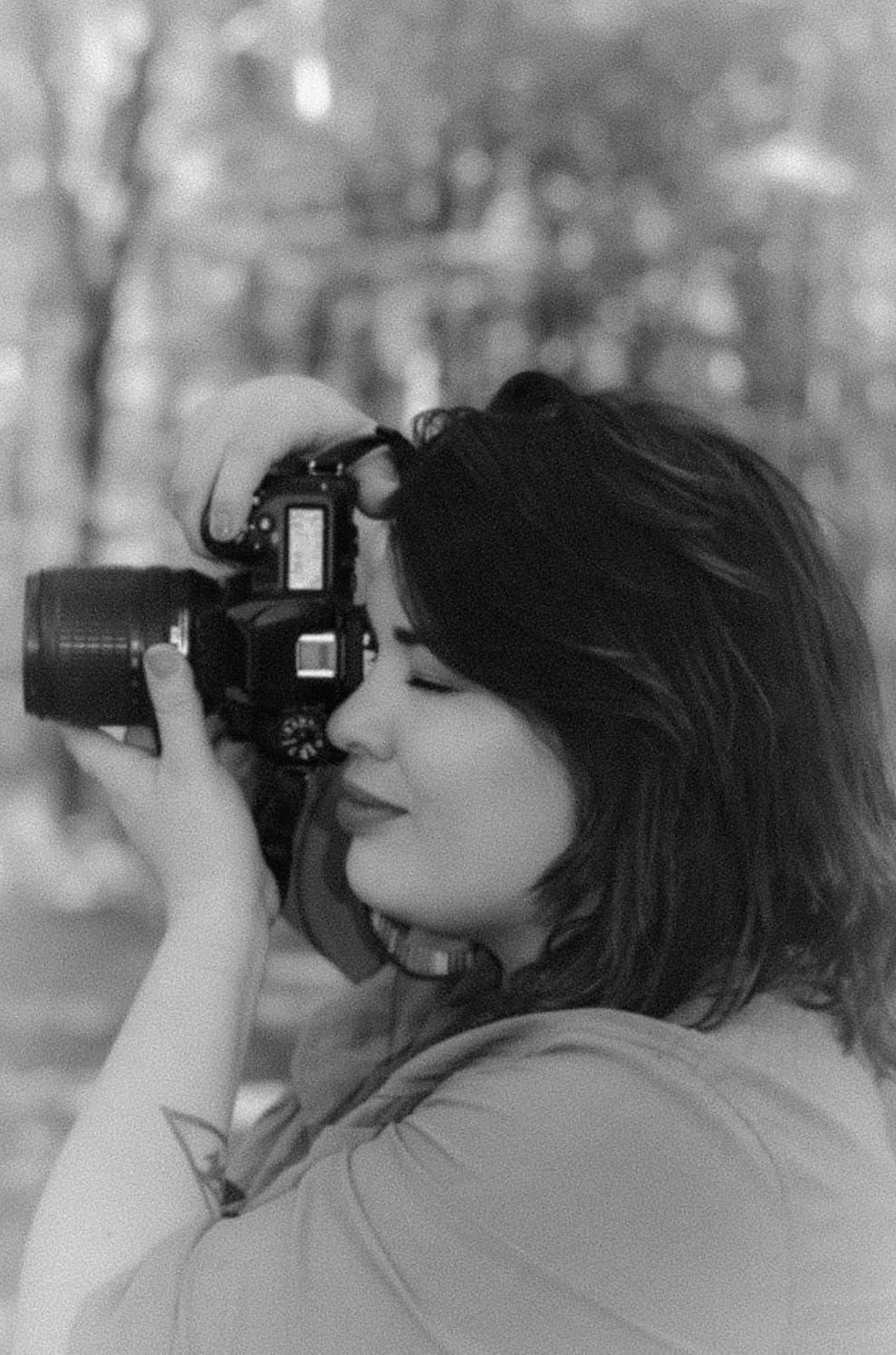 A woman photographs with a DSLR camera outdoors in a black and white portrait shot.