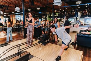 Group of friends enjoying bowling at a lively indoor bowling alley bar with lanes and spectators.