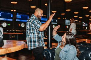 Two people high-fiving in a lively sports bar with TVs and warm lighting in the background.