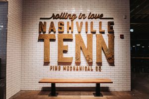 Nashville Tennessee rolling in love sign on white brick wall with wooden bench at Pine Mechanical Co.