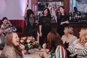 Women celebrating at a restaurant gathering, raising glasses and smiling around a flower-adorned table.