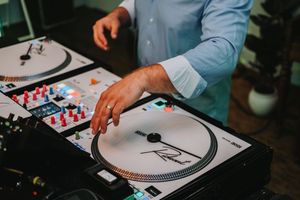DJ mixing music on turntables and DJ controller at an event, wearing a light blue shirt.