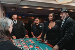Group of smiling guests enjoying a casino roulette table at an elegant evening event.