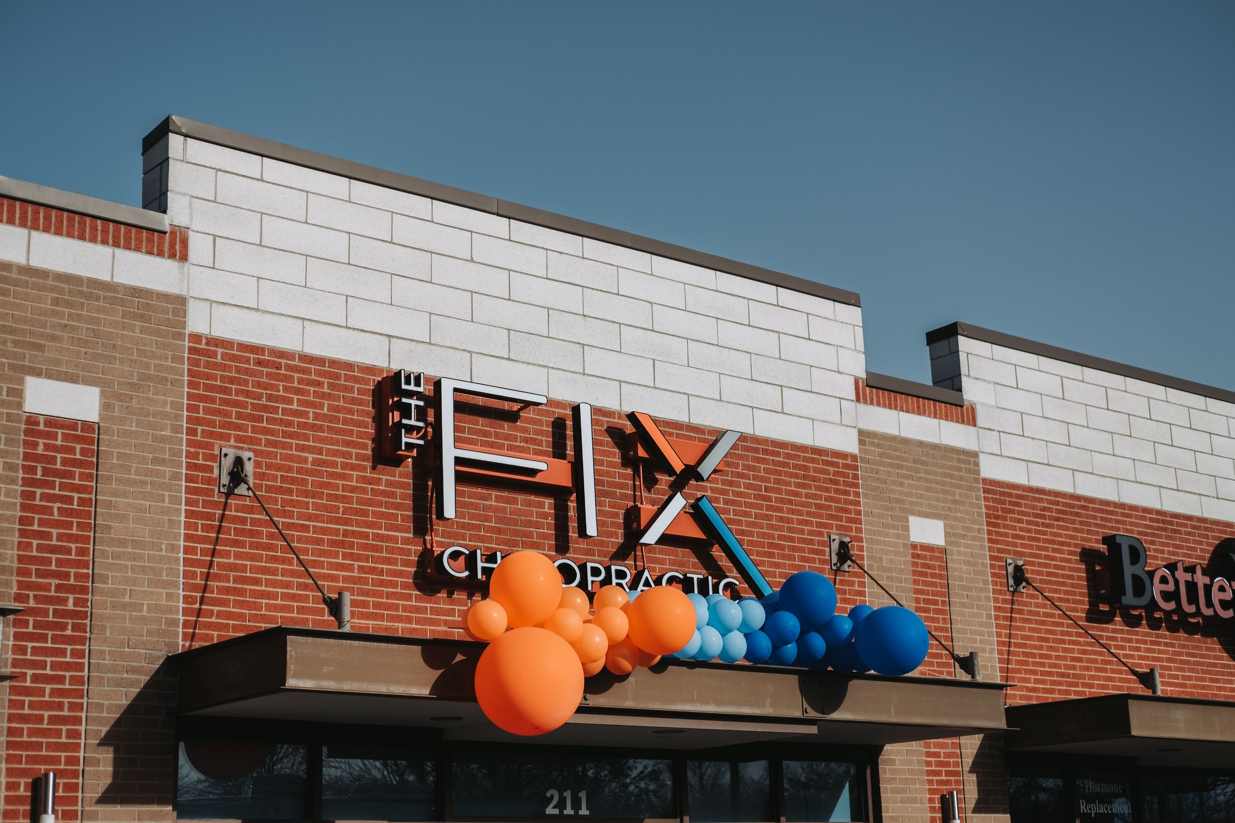 The Fix Chiropractic storefront decorated with colorful orange and blue balloons on a sunny day.