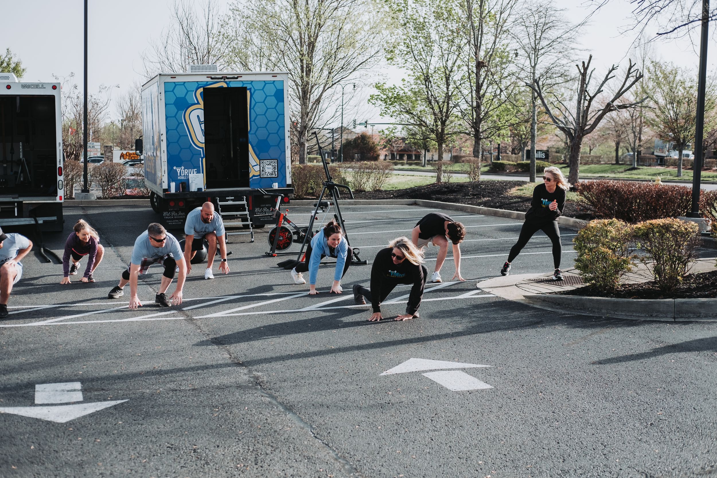 Group fitness class doing push-ups in a parking lot outdoors during a sunny spring day.