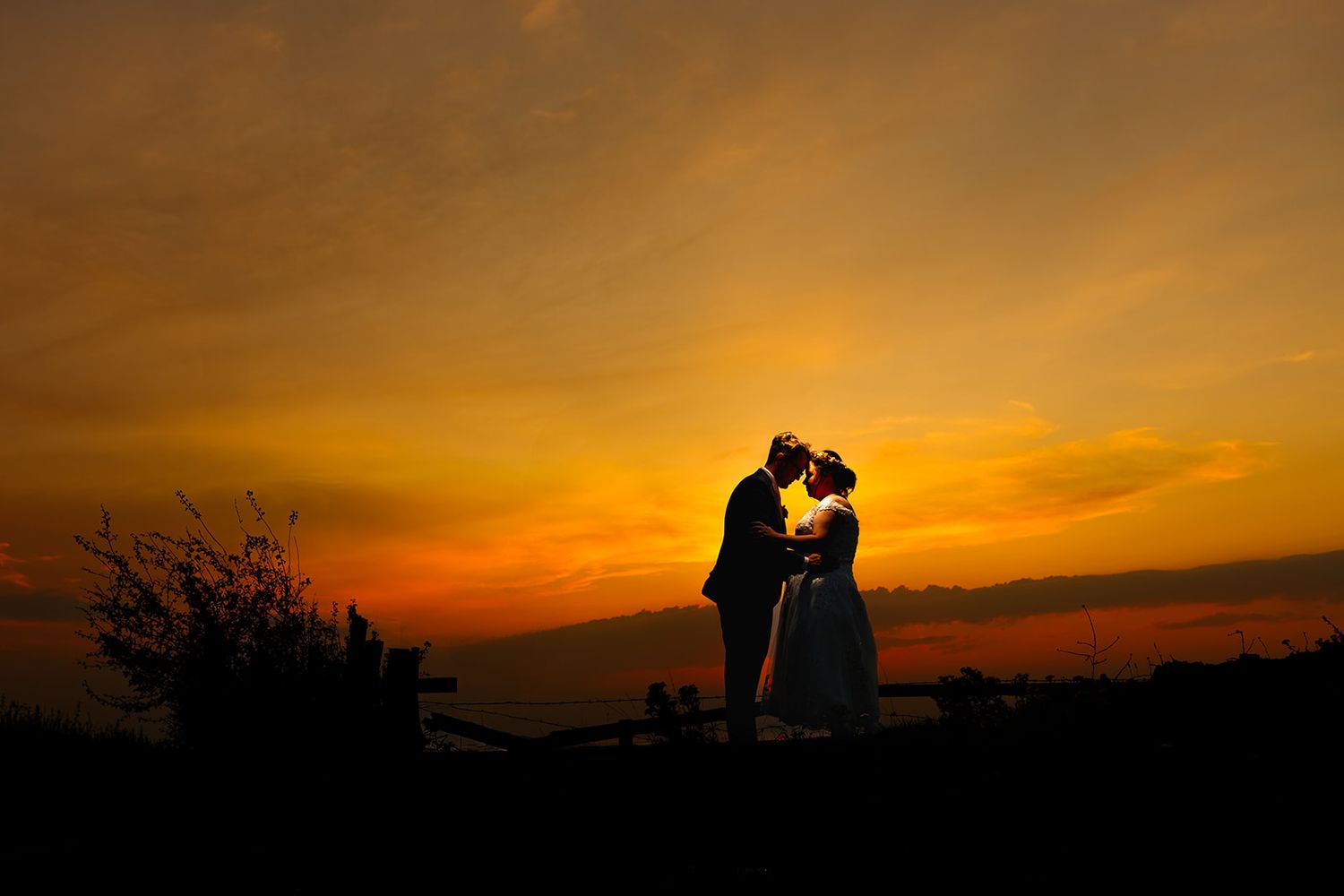 Silhouette of a romantic couple sharing a kiss at sunset with a vibrant orange and yellow sky backdrop.