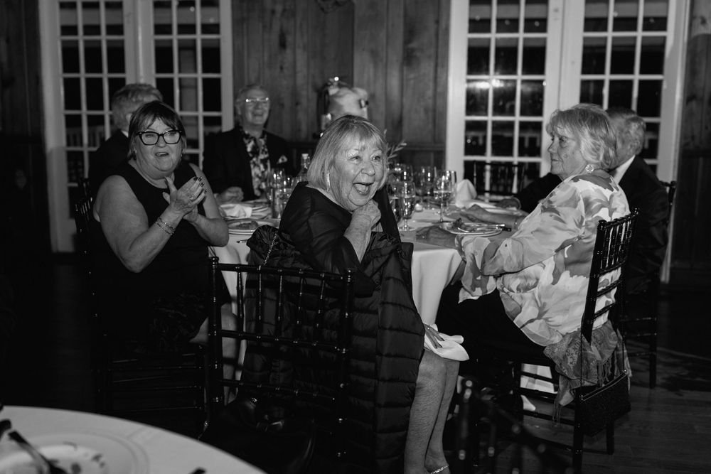 Black and white photo of women laughing and socializing at an elegant indoor dinner party event.