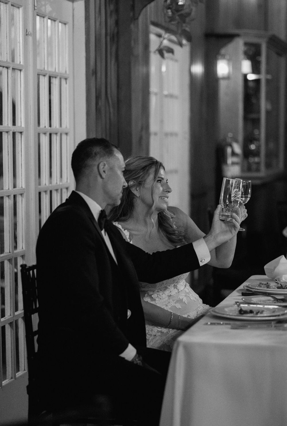 Black and white photo of a bride and groom toasting at their wedding reception dinner table.