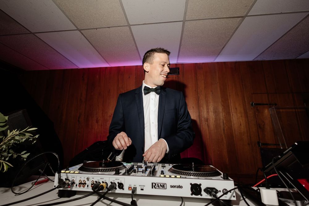 Smiling DJ in tuxedo mixing tracks on Rane turntables at an elegant evening event.
