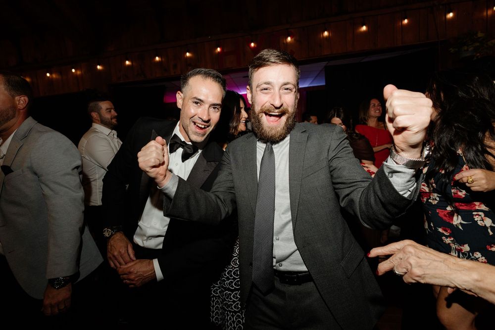 Two men in suits celebrating and dancing at a formal party or wedding reception event.