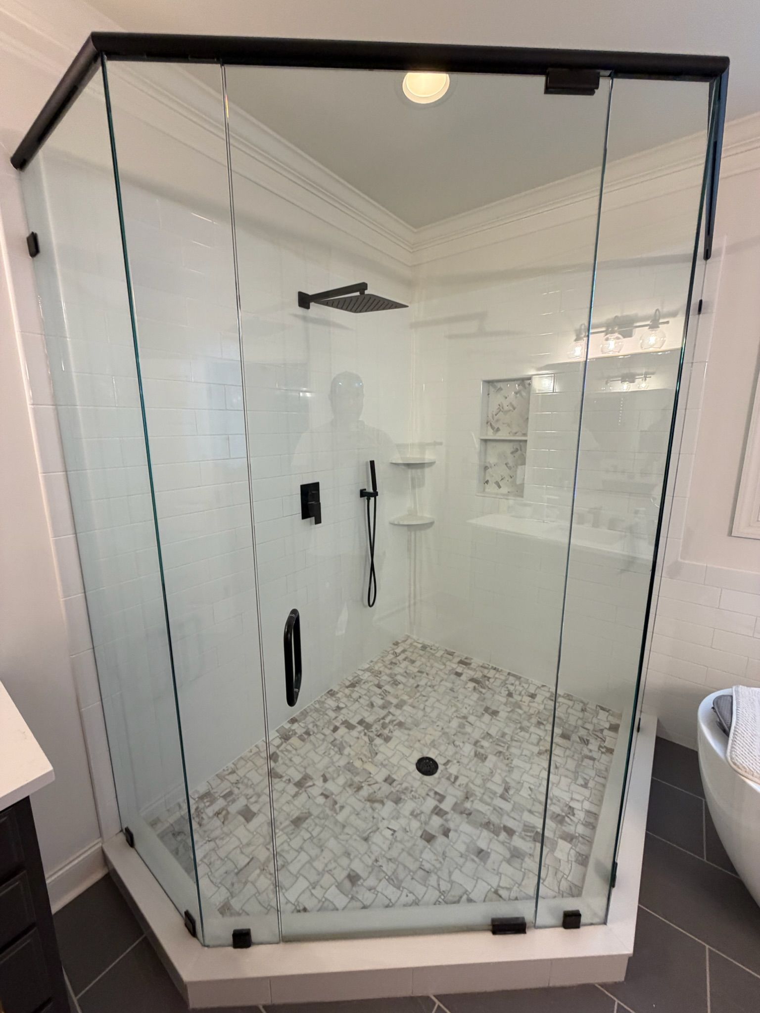 Frameless glass corner shower enclosure with white subway tiles and marble mosaic floor.