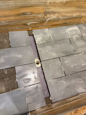Gray slate tiles being installed on a floor with a drain pipe visible in the center gap between tile sections.