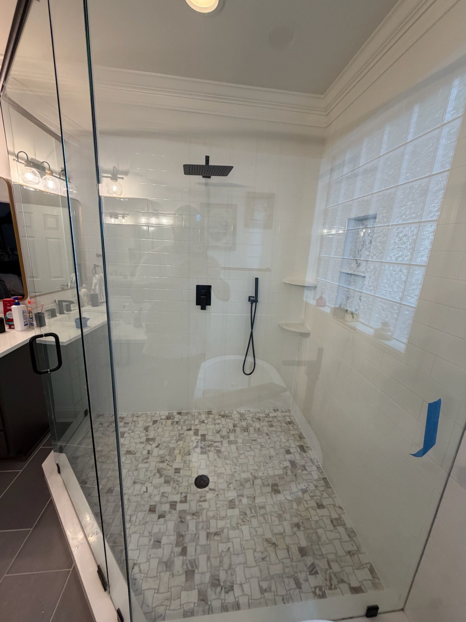 Modern walk-in shower with glass enclosure, matte black rain showerhead, mosaic tile floor, and glass block window.